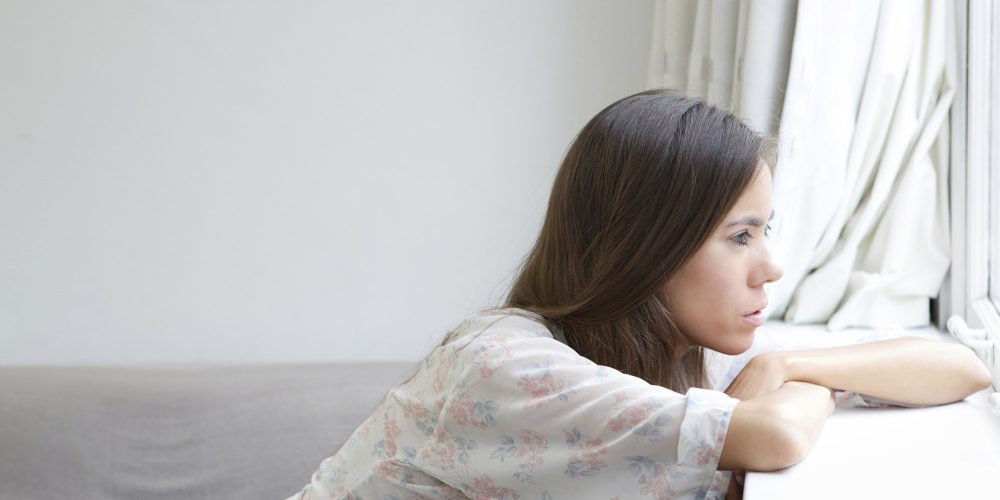 Young woman sitting alone looking out window